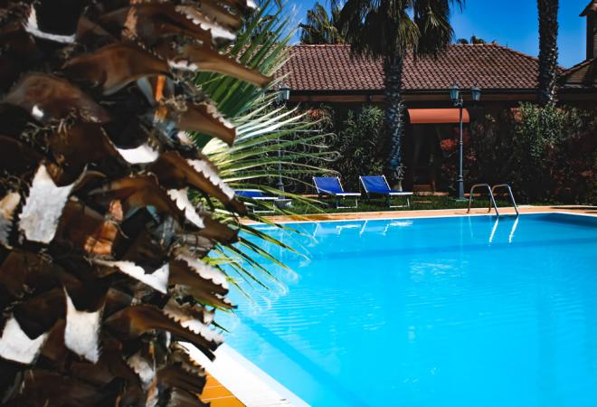 Piscina blu brillante, palme e lettini evocano relax estivo.
