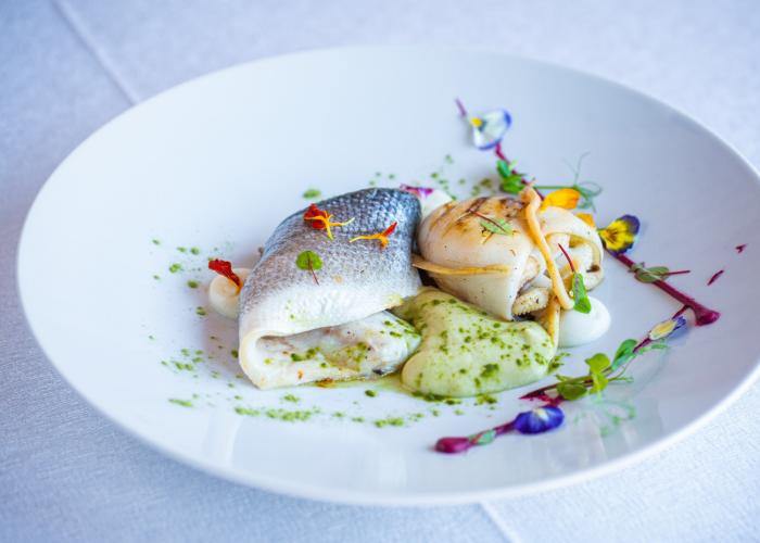 Piatti di pesce raffinati con decorazioni floreali e crema verde, eleganza gourmet.