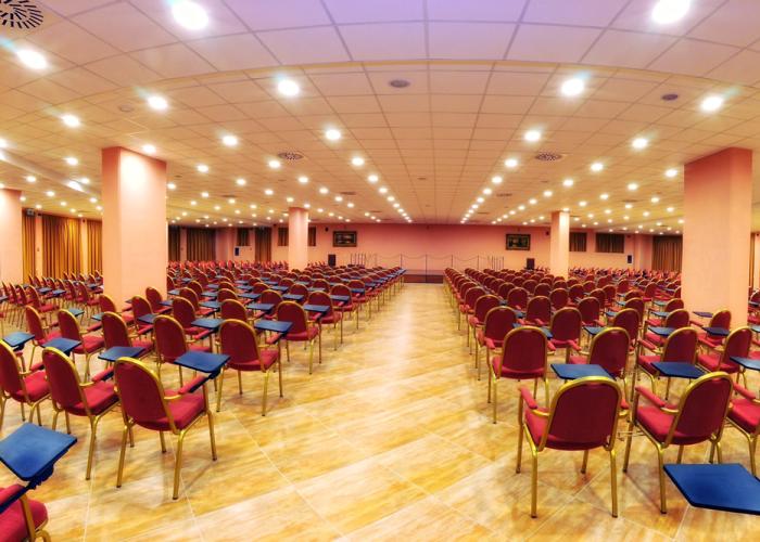 Bright conference room, orderly red chairs, atmosphere of anticipation and focus.